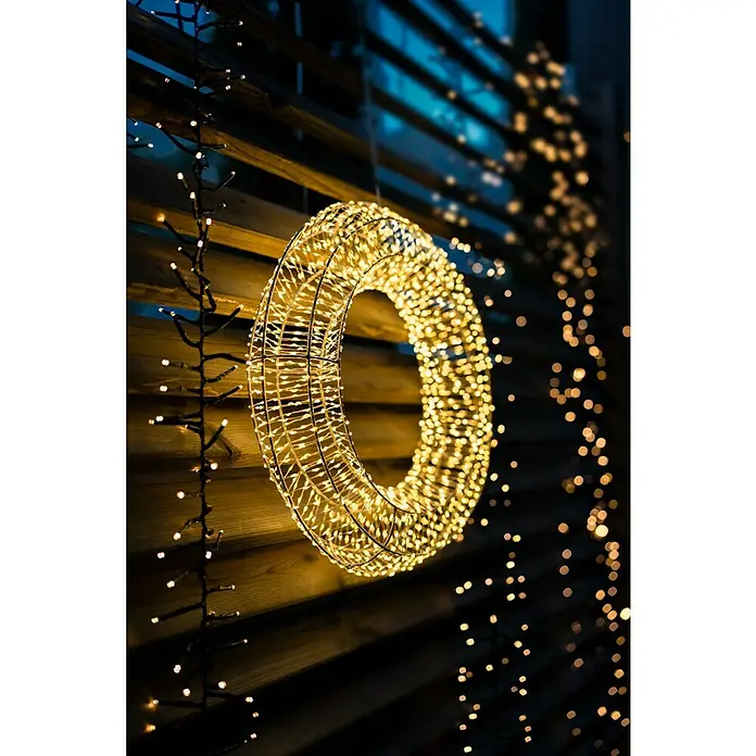 Tween Light Cadena de luces LED - Para exterior, Largo: 8,15 m, 768 ud., Funcionamiento en red, Color de luz: Blanco cálido - Primer plano de un adorno navideño LED redondo y luminoso colgado en una pared de madera con luces de cadena.