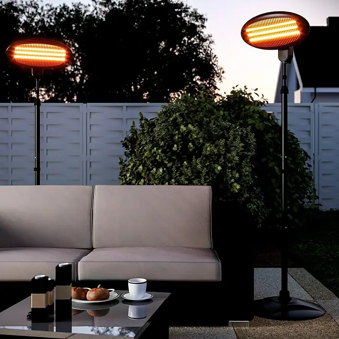 Voltomat HEATING Estufa de pie infrarrojos para exterior - 2.000 W, Negro - Dos calentadores de patio iluminan una terraza con un sofá y una mesa. Los calentadores proporcionan luz cálida y calor confortable al aire libre.