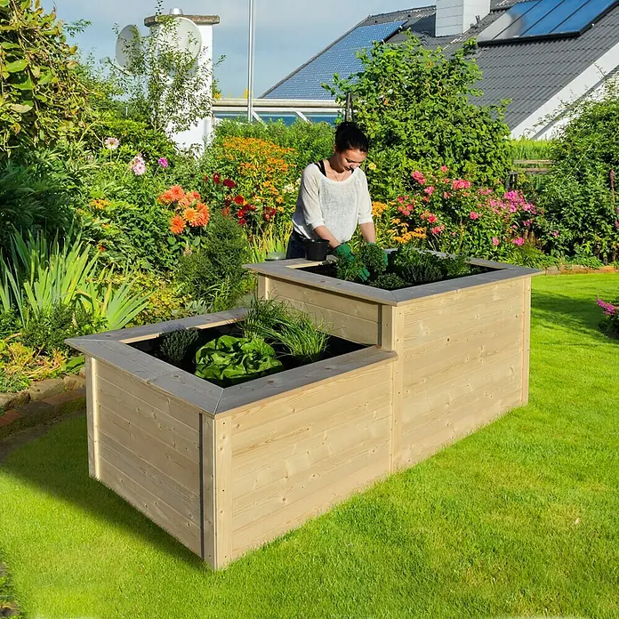 Weka Hochbeet - 205 x 79 x 81 cm, Holz, Natur, Stufenhochbeet - Bild eines zweistufigen Hochbeets aus Holz in einem Garten, in dem eine Frau gärtnert. Das Hochbeet ist bepflanzt und fügt sich gut in die grüne Umgebung ein.