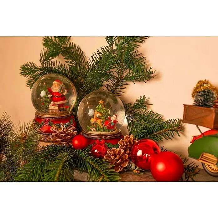 Schneekugel mit Spieluhr - Kunststoff, Weihnachtsmann - Zwei festliche Weihnachtsschneekugeln zwischen grünen Tannenzweigen, roten Kugeln und Tannenzapfen, eine Weihnachtsdeko.