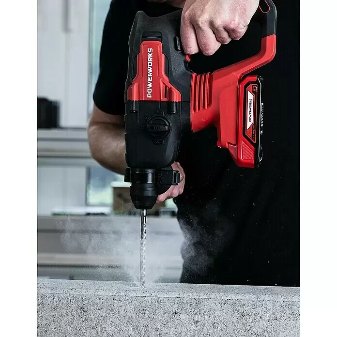 Powerworks Akku-Bohrhammer PD24SDS2 - 24 V, Ohne Akku, 2 J - Eine Person bohrt mit einem rot-schwarzen POWERWORKS Akku-Bohrhammer in eine Betonoberfläche, wodurch Staub entsteht.