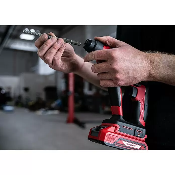 Powerworks Akku-Bohrhammer - 24 V, Ohne Akku, 1,2 J - Eine Person hält einen rot-schwarzen Akku-Bohrhammer und einen Metallbohrer, bereit, den Bohrer einzusetzen.