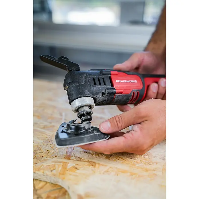 Powerworks Akku-Multifunktionswerkzeug P24MT - 24 V, Ohne Akku - Ein roter und schwarzer "Powerworks" Multifunktionswerkzeug mit einem dreieckigen Schleifaufsatz wird von Händen gehalten.