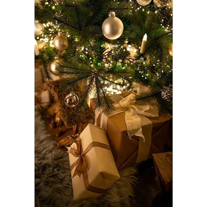 Velas de Navidad LED - 110 mm, Marfil, Color de luz: Blanco cálido, Número de bombillas: 20 ud., IP20 - Imagen atmosférica de un árbol de Navidad con regalos debajo, adornados con cintas, capturando el ambiente festivo.
