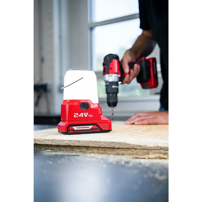Powerworks LED-Arbeitsleuchte P24LA500 - 24 V, Ohne Akku, 500 lm - Das Bild zeigt eine Powerworks 24V Akku-Arbeitsleuchte und einen Akku-Bohrschrauber auf einem Holztisch, ideal für Werkstattarbeiten.