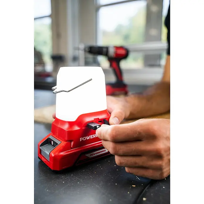 Powerworks LED-Arbeitsleuchte P24LA500 - 24 V, Ohne Akku, 500 lm - Nahaufnahme einer Powerworks Lampe, die an eine Stromquelle angeschlossen wird, mit einem roten Akkuschrauber im Hintergrund.
