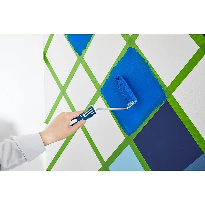 Frogtape Cinta de pintor - 41 m x 3,6 cm - El pintor está usando un rodillo para pintar un patrón de diamantes azules en una pared enmascarada con cinta verde.