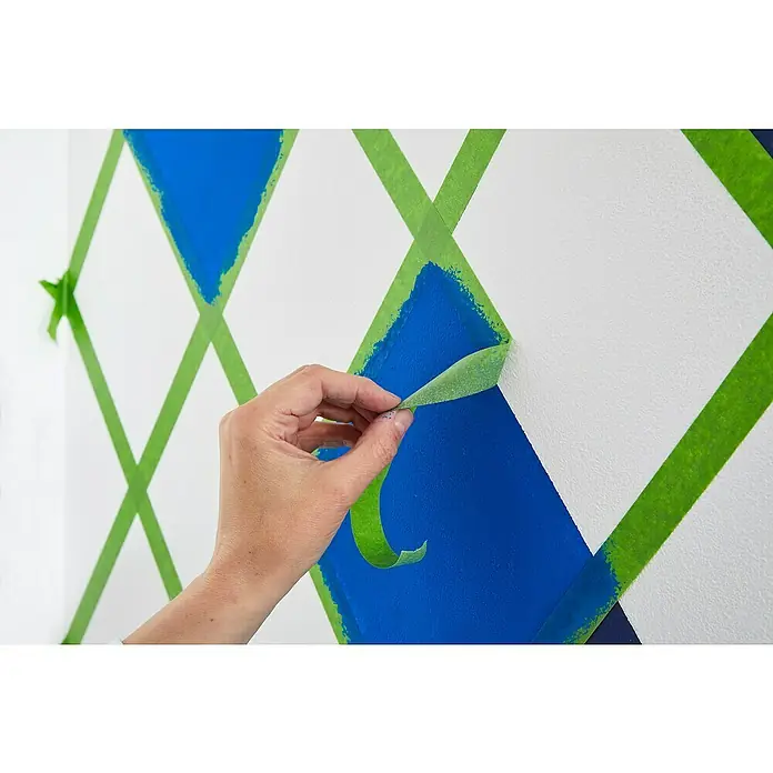 Frogtape Cinta de pintor - 41 m x 3,6 cm - Una persona retira cinta de pintor de una pared con diamantes pintados de azul, revelando un patrón geométrico limpio.