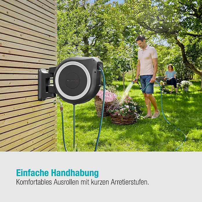 Gardena Wand-Schlauchbox RollUp M/L - Schlauchlänge: 25 m - Gartenszene mit einer Gardena Wand-Schlauchbox im Einsatz, die Blumen bewässert, während eine Person auf einer Bank entspannt.