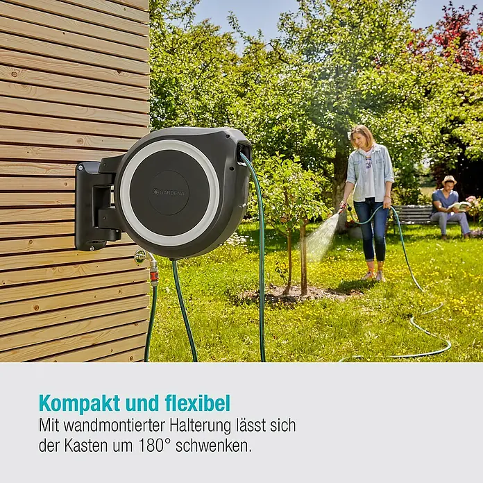 Gardena Wand-Schlauchbox RollUp L - Schlauchlänge: 30 m - Die Gardena Schlauchbox mit automatischer Aufrollfunktion an einer Holzwand. Im Hintergrund eine Frau beim Bewässern des Gartens.