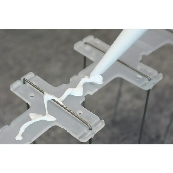 Altadex Sistema antipalomas - Largo: 200 cm, Acero - Primer plano de silicona blanca aplicada desde un cartucho sobre una pieza de plástico transparente con refuerzo metálico.