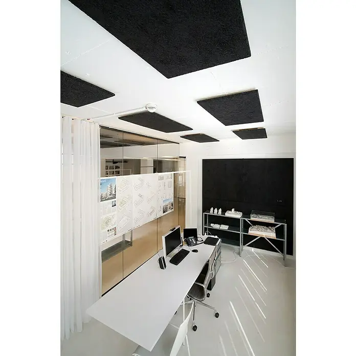 FibroTech Akustikplatte Multi Fein - Fein Schwarz, 1.200 x 600 x 25 mm, 0,72 m² - Ein minimalistisches Büro mit Akustikplatten an der Decke, einem langen Schreibtisch und einem Regal mit Architekturmodellen.