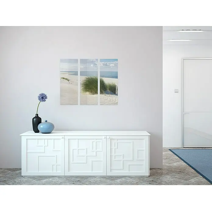 Glasbild - Seaside Idyll, B x H: 90 x 80 cm, 3 -tlg. - Ein weißes Sideboard mit geometrischen Mustern steht im Raum, darüber hängt ein dreiteiliges Bild. Dekorativ sind blaue Blumen und Vasen.