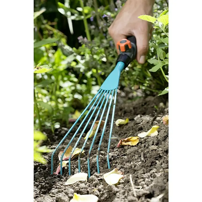 Gardena Combisystem Drahthandfeger - Arbeitsbreite: 12 cm, Edelstahl - Nahaufnahme eines blauen Fächerschiebers, der Blätter in einem Gartenbeet entfernt.