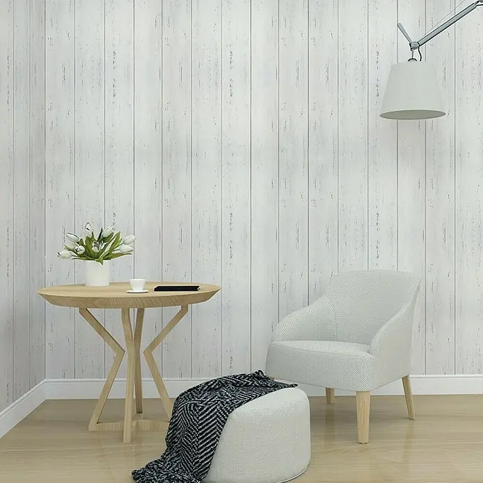 Papel pintado vinílico adhesivo Lineawall - Tablero blanco, 90 cm x 2,8 m - Una habitación acogedora con un sillón, otomana, mesa con flores y una lámpara contra una pared con paneles de madera.