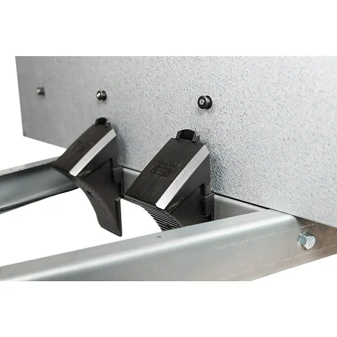 Stema Anhänger Mini 750G R10 mit Stützrad u. Stoßdämpfer - Nutzlast: 621 kg, Einachser, Kasteninnenmaß: 134 x 108 x 26,5 cm, Gebremst - Nahaufnahme von zwei schwarzen AL-KO-Bremskeilen, die an einer silbernen Metallkonstruktion befestigt sind und ein sicheres Feststellen gewährleisten.