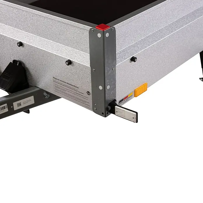 Stema Anhänger Basic 1000 mit Abstellstützen u. Gitteraufsatz - Nutzlast: 768 kg, Gebremst - Nahaufnahme eines Anhängers mit Metalloberfläche, Warnschild und Reflektor für den Straßenverkehr.