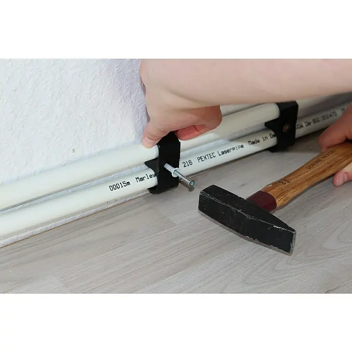 Marley Leistenclip - 4 Stk. - Befestigung von PEXTEC Laserpipes mit einer Rohrschelle an einer Wand mit einem Hammer und Schraube.
