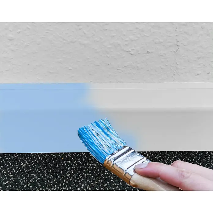 Marley Außenecke - Esche Weiß - Nahaufnahme eines Pinsels, der eine weiße Fußleiste mit hellblauer Farbe streicht, vor einem Hintergrund einer weißen Wand.