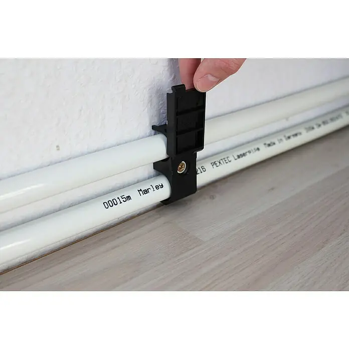 Marley Leistenclip - 4 Stk. - Nahaufnahme von Rohren, die mit einer schwarzen Rohrschelle an einer Wand befestigt sind. Die Rohrschelle hält zwei weiße Rohre parallel.