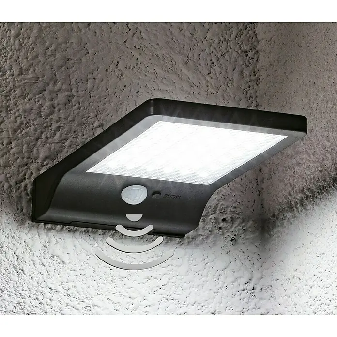 LED-Solar-AußenwandleuchteBewegungsmelder, 3 W, 300 lm, Kaltweiß, Schwarz - Nahaufnahme einer Solarleuchte mit Bewegungsmelder an einer strukturierten Wand, die Lichtstrahlen aussendet.