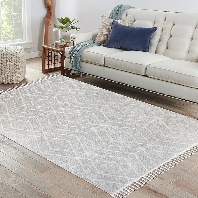 Alfombra de pelo corto Claudia Rombos - Crema, 60 x 110 cm, 100% poliéster - Una alfombra gris con un estampado geométrico y flecos se encuentra en una sala de estar acogedora con un sofá.