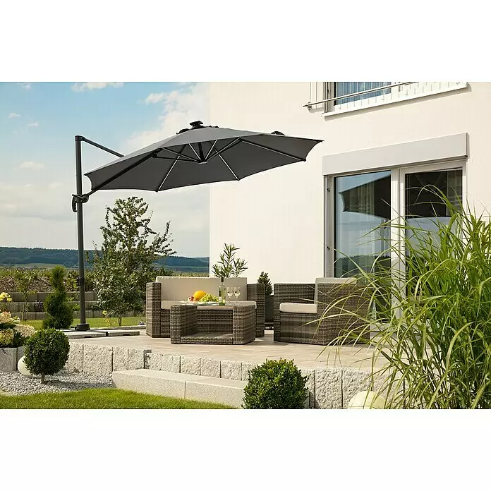 Schneider Ampelschirm rund Rhodos Blacklight - Anthrazit, Durchmesser Bespannung: 300 cm - Großer anthrazitfarbener Ampelschirm mit Metallgestell, spendet Schatten über Rattan-Gartenmöbeln auf einer sonnigen Terrasse.