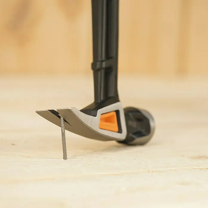 Fiskars Universalhammer XL - Gewicht Kopf: 570 g, Länge: 390 mm - Nahaufnahme eines Zimmermannshammers, der einen Nagel aus einem Holzbrett zieht, wobei der Fokus auf dem Werkzeug und seiner Funktion liegt.