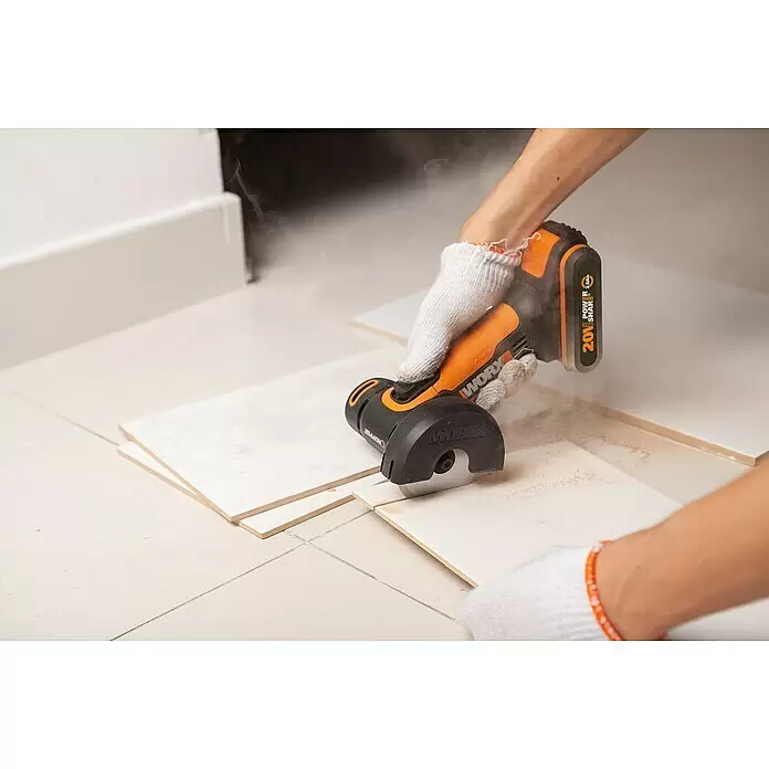 Worx PowerShare 20V Akku-Trennschleifer WX801 - 1 Akku, 2 Ah, Durchmesser Scheibe: 76 mm - Person schneidet mit einer orange-schwarzen Akku-Minikreissäge weiße Fliesen, dabei entsteht Staub.