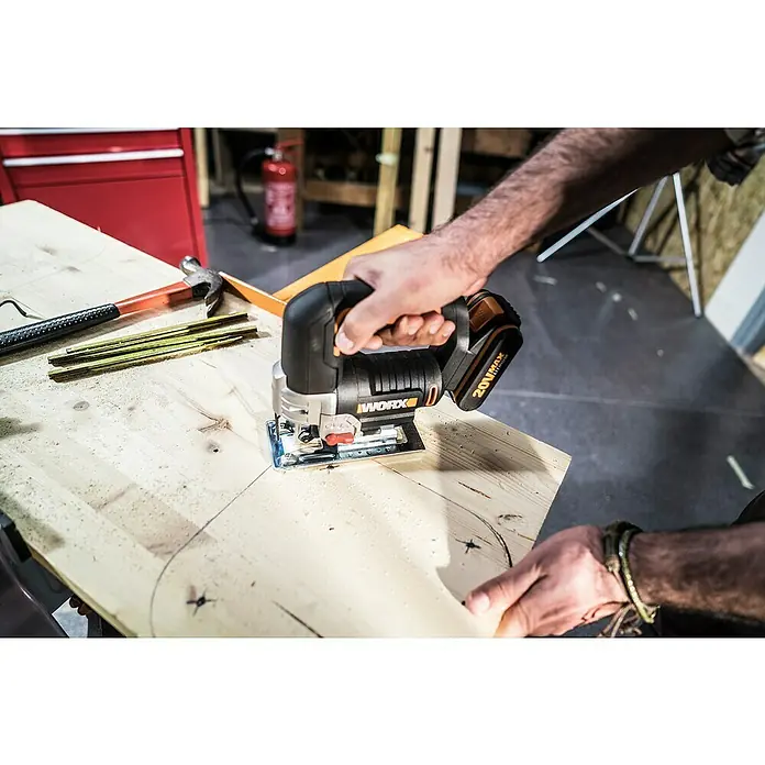 Worx PowerShare 20V Akku-Stichsäge WX543 - 20 V, 1 Akku, 2 Ah, Leerlaufhubzahl: 0 /min - 2.600 /min - Ein Mann benutzt eine WORX Stichsäge, um ein Holzstück zu bearbeiten, wobei Werkzeuge wie Hammer und Zollstock daneben liegen.