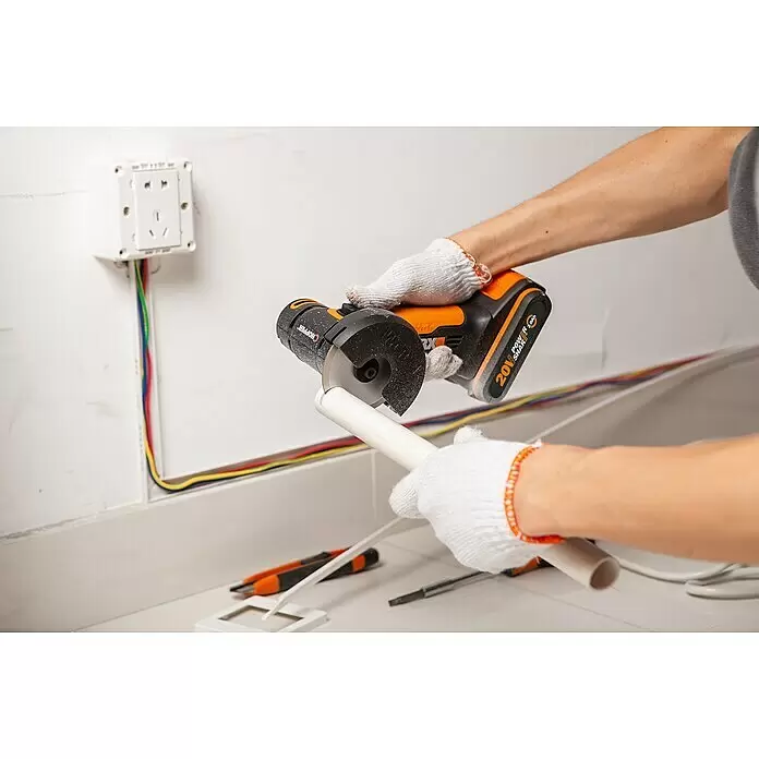 Worx PowerShare 20V Akku-Trennschleifer WX801 - 1 Akku, 2 Ah, Durchmesser Scheibe: 76 mm - Person mit Handschuhen schneidet ein weißes PVC-Rohr mit einem orange-schwarzen Akku-Trennschleifer.