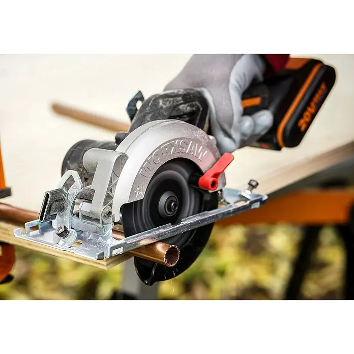 Worx PowerShare 20V Akku-Handkreissäge WX531.9 - 20 V, Ohne Akku, Leerlaufdrehzahl: 6.900 U/min - Eine Akku-Handkreissäge WORKSAW schneidet ein Kupferrohr. Das Werkzeug ist silberfarben mit rotem Hebel und schwarzem Griff.
