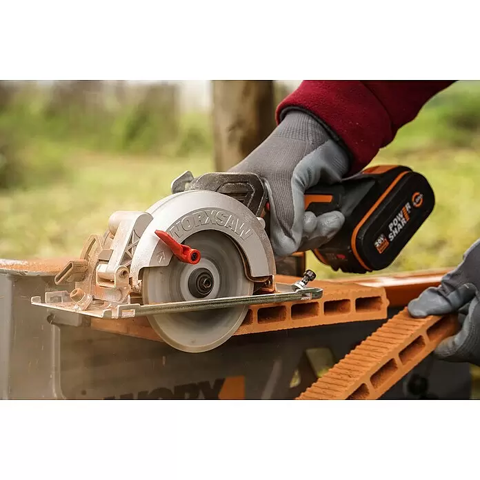 Worx PowerShare 20V Akku-Handkreissäge WX531.9 - 20 V, Ohne Akku, Leerlaufdrehzahl: 6.900 U/min - Behandschuhte Hände bedienen eine silberne und rote Akku-Kreissäge, die einen orangefarbenen Hohlziegel schneidet. Das Werkzeug hat einen schwarz-orangen Akku.