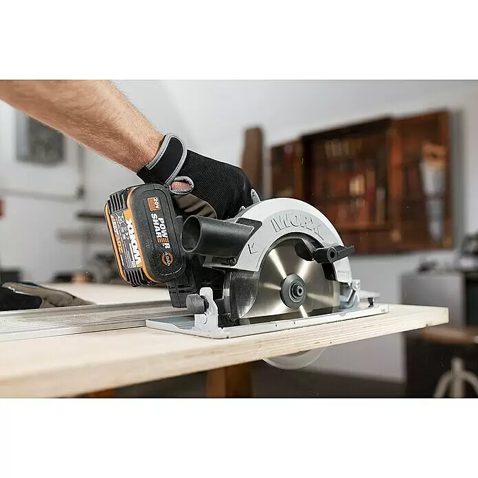 Worx PowerShare 20V Akku-Handkreissäge WX520.9 - 20 V, Ohne Akku, Durchmesser Scheibe: 185 cm - Behandschuhte Hand schneidet Holzbrett mit silber-schwarzer Akku-Kreissäge (orangefarbener Akku). Holzstaub sichtbar.