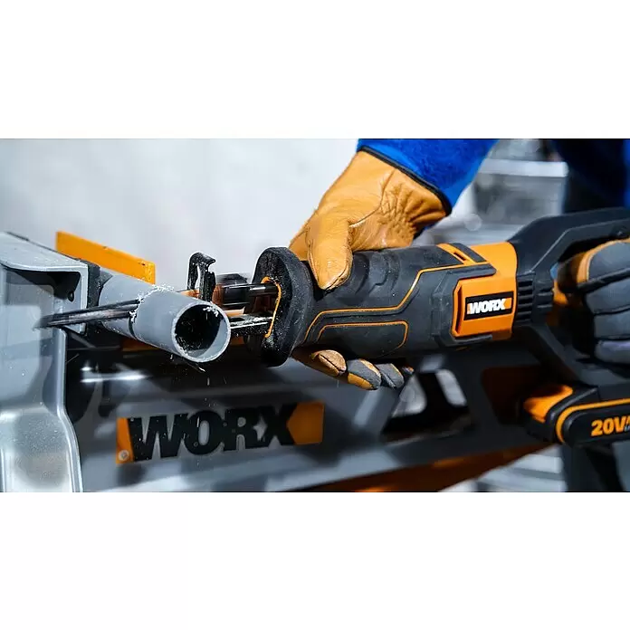 Worx PowerShare 20V Akku-Säbelsäge WX516.9 - 20 V, Ohne Akku, Hublänge: 29 mm - Person mit braunen Handschuhen schneidet mit einer orange-schwarzen WORX Säbelsäge ein graues PVC-Rohr in einem grauen Ständer.