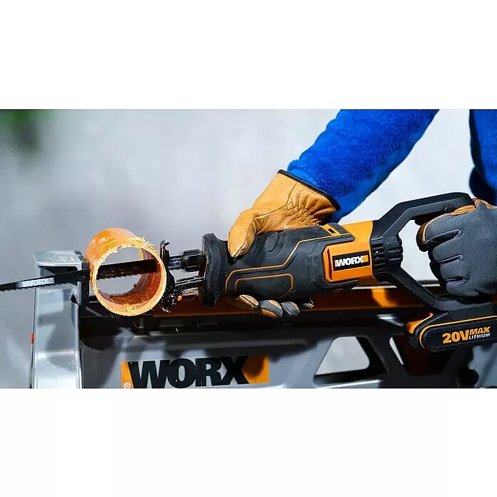Worx PowerShare 20V Akku-Säbelsäge WX516.9 - 20 V, Ohne Akku, Hublänge: 29 mm - Behandschuhte Hände bedienen eine orange-schwarze WORX-Säbelsäge, die ein orangefarbenes Rohr auf einem Werkständer schneidet.