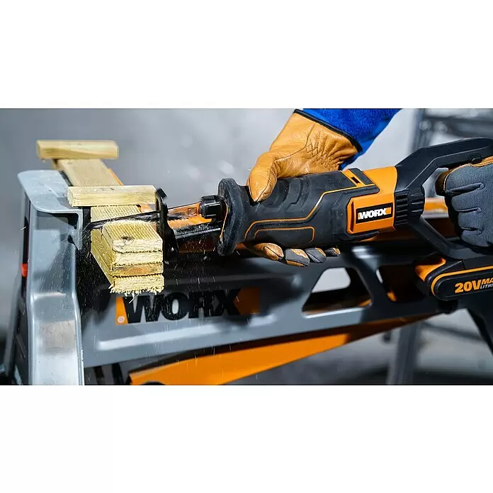 Worx PowerShare 20V Akku-Säbelsäge WX516.9 - 20 V, Ohne Akku, Hublänge: 29 mm - Eine orange-schwarze Worx Säbelsäge, von einer behandschuhten Hand gehalten, schneidet Holz auf einem Worx Sägebock, mit fliegenden Spänen.