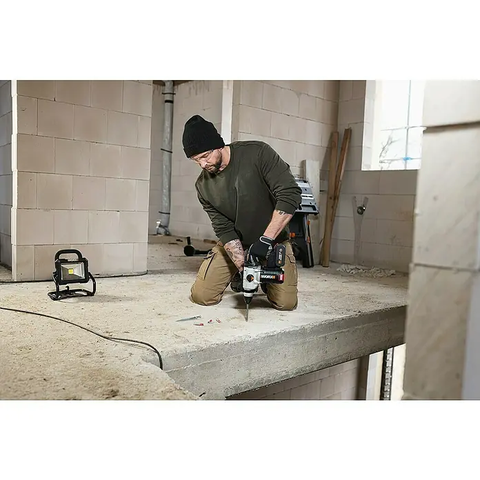 Worx PowerShare 20V Akku-Bohrhammer WX380.9 - 20 V, Ohne Akku, 2,2 J - Ein Mann kniet und bohrt mit einem Worx-Bohrhammer in einen Betonboden, während eine Arbeitsleuchte die Szene erhellt.