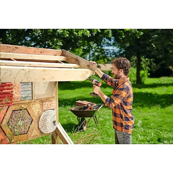 Worx PowerShare 20V Akku-Schlagbohrschrauber SlammerDrill WX354.9 - 20 V, Ohne Akku, Li-Ionen, 2 Ah, 60 Nm - Ein Mann in einem karierten Hemd befestigt mit einem schwarz-rot-orangen Akkubohrschrauber ein Holzbrett an einer Gartenkonstruktion.
