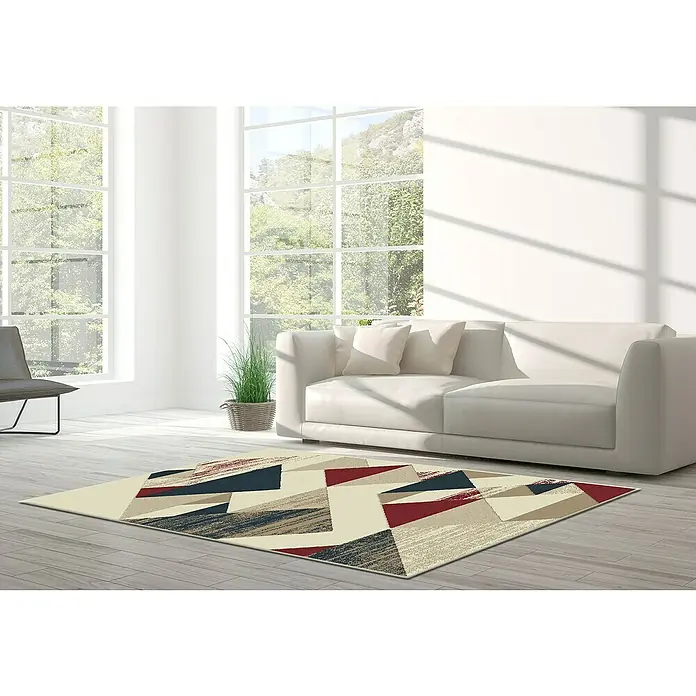 Alfombra de pelo corto Alpes - Granate, 100% polipropileno - Una alfombra elegante con patrones geométricos en rojo, azul y beige se encuentra en una sala de estar moderna y luminosa.