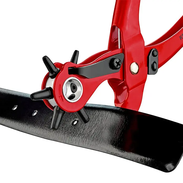 Knipex Lochzange - Länge: 22 cm, Stahl - Nahaufnahme einer roten Revolverlochzange beim Lochen eines schwarzen Ledergürtels. Werkzeug und Lederaccessoire im Fokus.