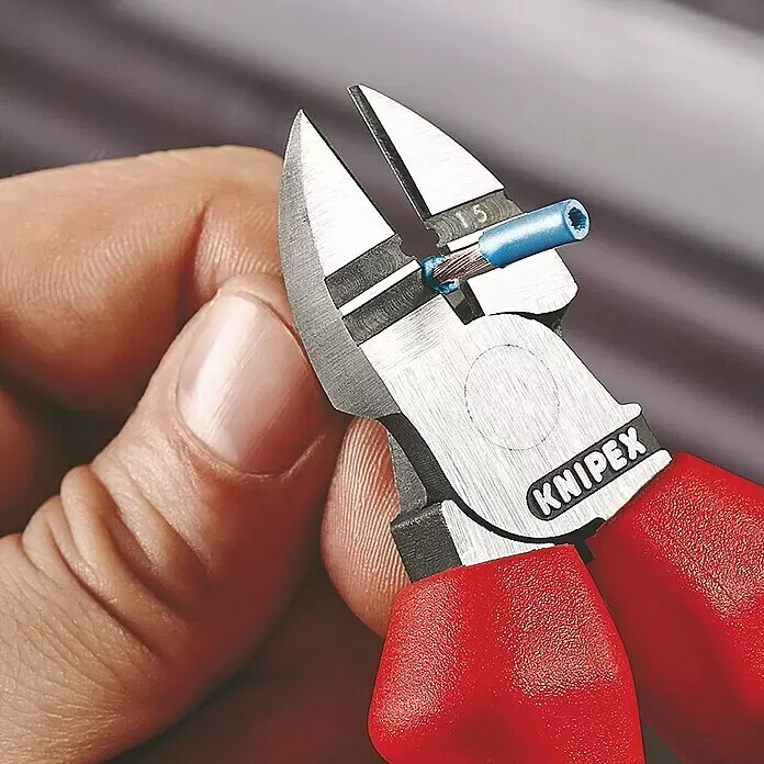 Knipex Seitenschneider - Länge: 16 cm, Härte Schneide: 60 HRC - Eine Hand hält Knipex Seitenschneider mit roten Griffen, die ein blaues isoliertes Kabel abisolieren.