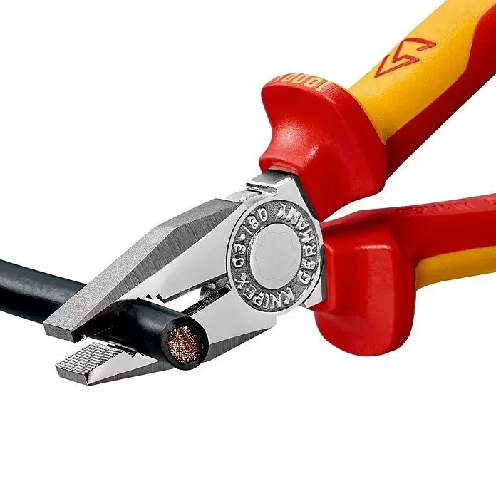 Knipex Kombizange - Länge: 18 cm, Ölgehärtet - Rote und gelbe isolierte Zange mit silbernen Backen, die ein schwarzes Elektrokabel schneidet und Kupferlitzen freilegt.