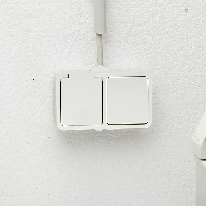 Voltomat Blueline Feuchtraum-Schalterkombination - Weiß, Ausrichtung Schalterprogramm: Horizontal, Aufputzmontage, IP54 - Eine Doppelsteckdose in Weiß an einer weißen Wand mit einer Kabelverbindung.