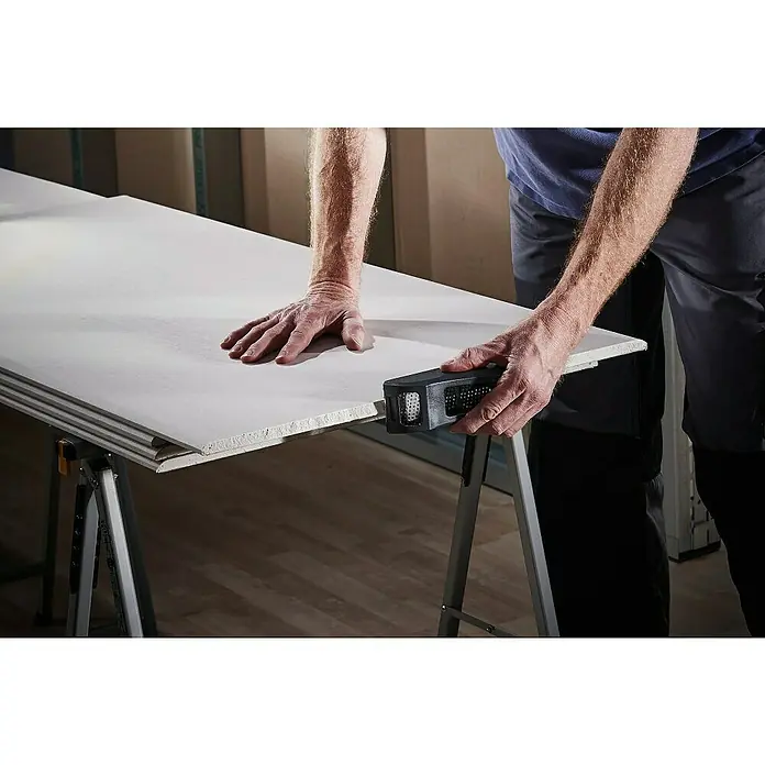 Wolfcraft Cepillo Surform manual 4013000 - Plástico - Una persona utiliza un cepillo de cantos para alisar el borde de una placa de yeso que descansa sobre dos caballetes.
