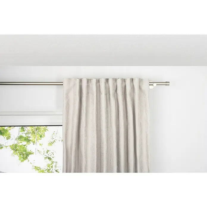 Verdunkelungsvorhang Dim - B x H: 135 x 300 cm, 100 % Polyester, Sand - Ein grauer Vorhang hängt an einer silbernen Gardinenstange vor einem Fenster und verleiht dem Raum eine elegante Note. Die dezenten Falten sorgen für ein harmonisches Gesamtbild.