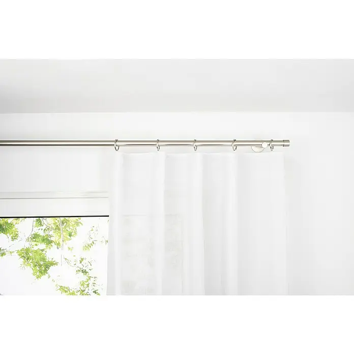 Schlaufenschal Breeze - B x H: 135 x 300 cm, 100 % Polyester, Weiß - Ein silberner Vorhang hängt an einer Gardinenstange mit Ringen, die an einer weißen Wand befestigt ist. Ein Fenster befindet sich links vom Vorhang.