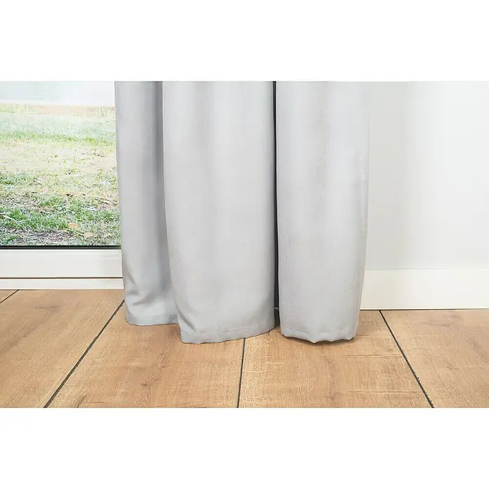 Verdunkelungsvorhang Dim - B x H: 135 x 300 cm, 100 % Polyester, Grau - Nahaufnahme von grauen Verdunkelungsvorhängen, die elegant auf einem Holzboden drapiert sind und ein Fenster teilweise verdecken.