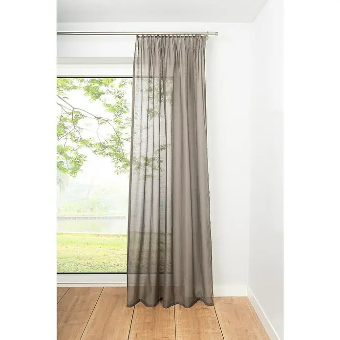 Schlaufenschal Soft - B x H: 135 x 300 cm, 100 % Polyester, Taupe - Ein grauer Vorhang hängt vor einem Fenster und sorgt für Privatsphäre und sanftes Licht im Raum. Der Stoff ist leicht transparent.