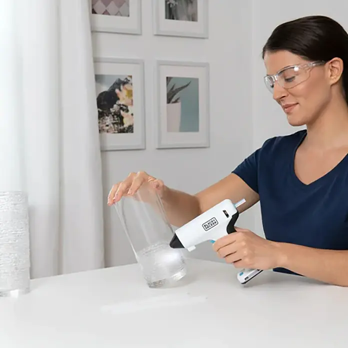 Black+Decker Pistola termoencoladora con batería BCGL115 3,6V-Li - 3,6 V - Mujer usando una pistola de pegamento Black+Decker para un proyecto DIY con un jarrón de vidrio, creando decoraciones únicas.